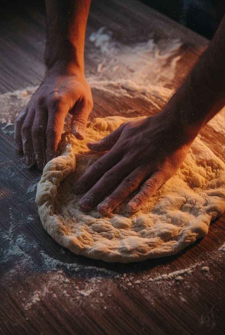 Handen bestoven met bloem kneden Napolitaans pizzadeeg op een donker werkblad.